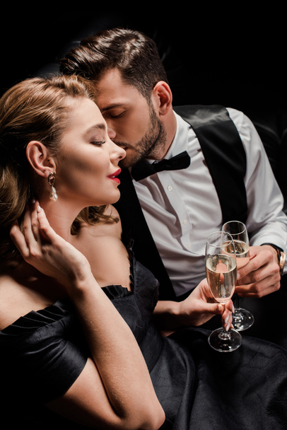 stylová, svůdná žena a elegantní muž cinkání sklenice šampaňského izolované na černé - Fotografie, Obrázek
