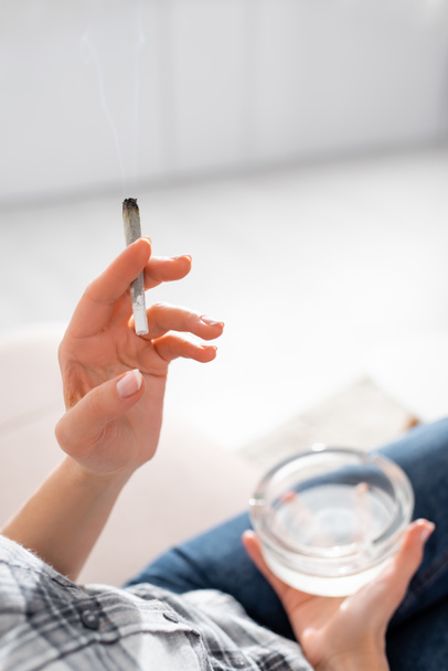 cropped view of mature woman holding joint with legal marijuana and ashtray  - Fotó, kép