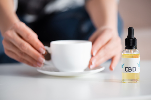 cropped view of mature woman touching cup of tea near bottle with cbd lettering - Φωτογραφία, εικόνα