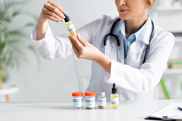 cropped view of doctor in white coat holding bottle with cbd lettering  - Fotografie, Obrázek