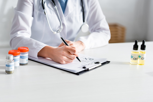обрезанный взгляд врача, выписывающего рецепт рядом с бутылками с медицинским каннабиса и CBD
  - Фото, изображение