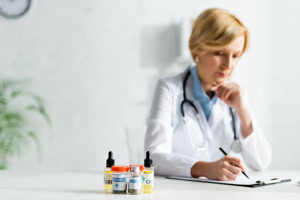 selective focus of bottles with medical cannabis and cbd near mature doctor writing prescription  - Fotografie, Obrázek