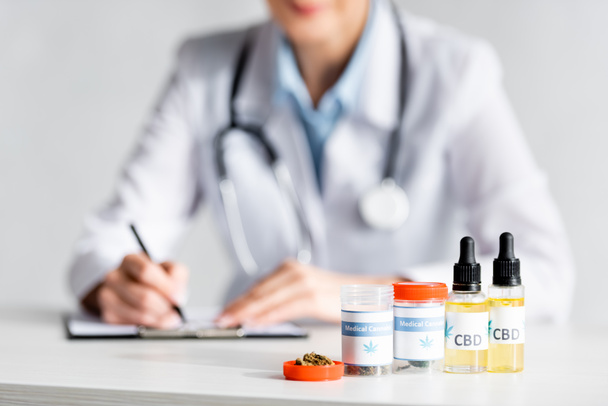 selective focus of dried marijuana, bottles with cbd and medical cannabis lettering near doctor writing prescription  - Photo, Image