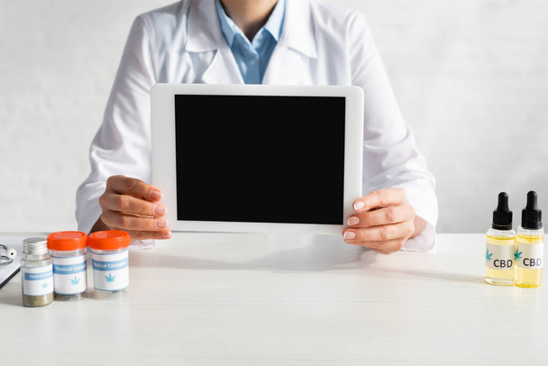 vista recortada do médico segurando tablet digital com tela em branco perto de garrafas com cbd e letras cannabis medicinal na clínica
  - Foto, Imagem