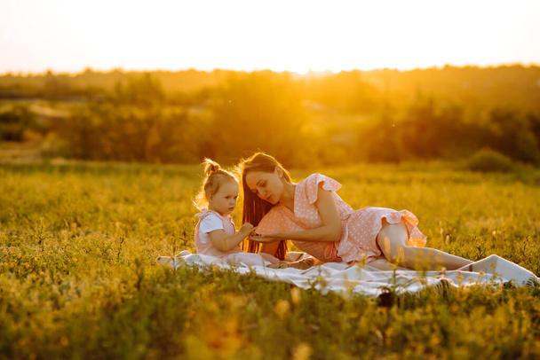 Anne ve küçük kızı gün batımında bir yaz parkında birlikte oynuyorlar. Küçük çocuklu mutlu bir anne güneşli bir alanda eğleniyor. Öpücükler ve sarılmalar. Mutlu aile kavramı..  - Fotoğraf, Görsel