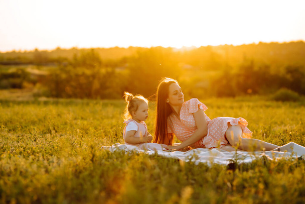Mère et petite fille jouent ensemble dans un parc d'été au coucher du soleil. Maman heureuse avec un petit enfant qui s'amuse sur un champ ensoleillé. Bisous et câlins. Le concept d'une famille heureuse
.  - Photo, image
