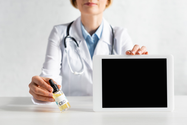 καλλιεργημένη άποψη του ώριμου γιατρού σε λευκό παλτό κρατώντας ψηφιακό δισκίο με λευκή οθόνη και μπουκάλι με cbd γράμματα  - Φωτογραφία, εικόνα