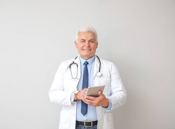 Portrait of male doctor with tablet computer on grey background - Photo, Image