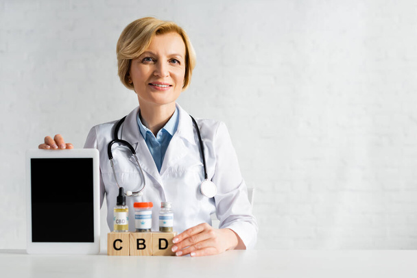 mature doctor holding digital tablet with blank screen near cubes with cbd lettering and drugs  - Fotografie, Obrázek