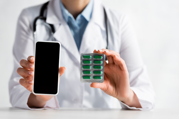 vista ritagliata del medico maturo che tiene smartphone con schermo bianco e blister con pillole
  - Foto, immagini