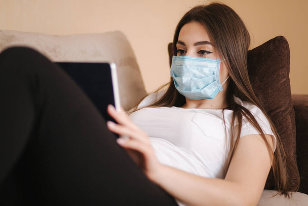Een vrouw met een beschermend masker die thuis werkt tijdens het Coronavirus. Vrouw zelf geïsoleerd thuis in de kamer. Blijf thuis. - Foto, afbeelding