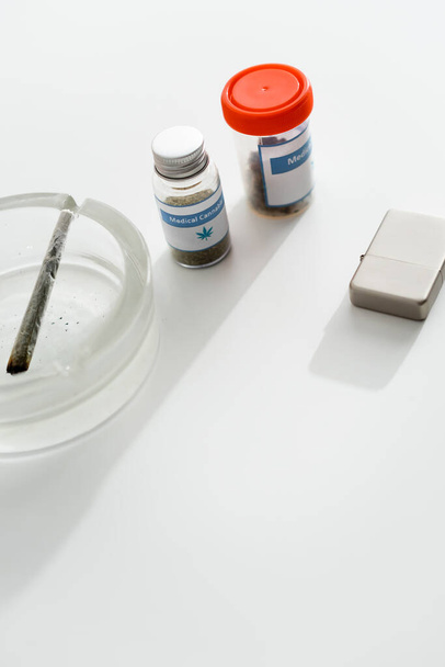 Flaschen mit medizinischem Cannabis nahe Feuerzeug, Aschenbecher und Joint mit legalem Marihuana  - Foto, Bild