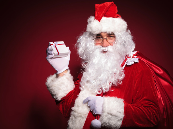 вид сбоку на Санта-Клауса, держащего в руках маленькую подарочную коробку
 - Фото, изображение