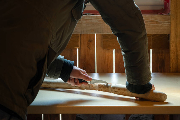 Процесс изготовления деревянной походки в помещении во время карантина. Вырезание деревянной палки на столе ножом - Фото, изображение