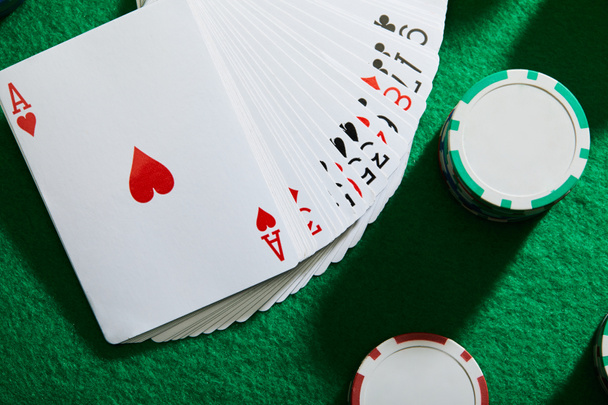 Top view of pack of cards with casino chips on green background - Photo, Image