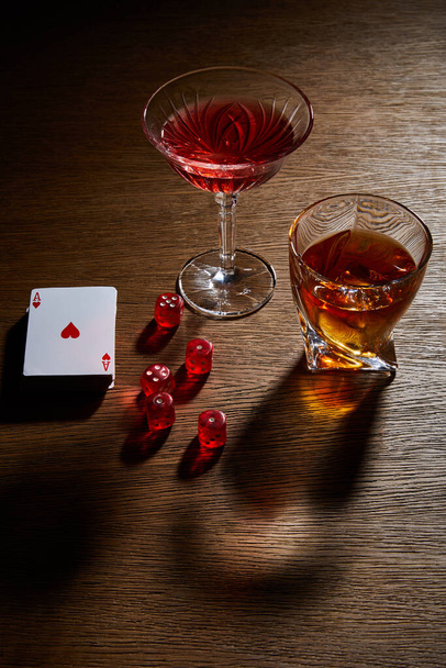 High angle view of glasses of cognac and cocktail near deck of cards and dice on wooden background - Foto, afbeelding