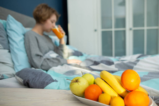 girl relaxes in the bedroom and drinks orange juice - Фото, изображение
