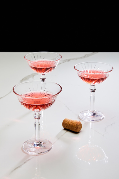 Glasses of cocktail and cork on white surface isolated on black - Photo, Image