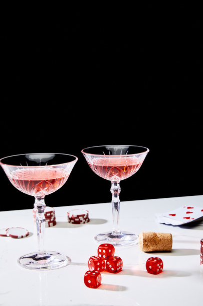 Glasses of cocktail, dice, cork, casino chips and pack of cards on white surface isolated on black - Fotoğraf, Görsel