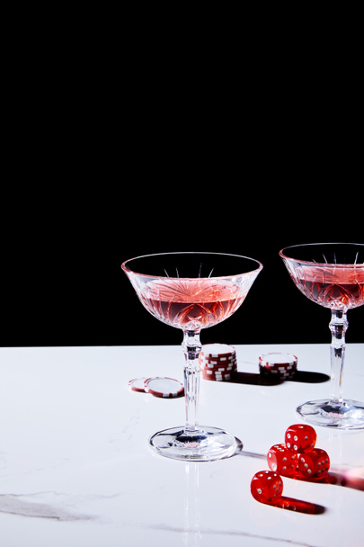 Glasses of cocktail, casino chips and dice on white surface isolated on black - Photo, Image