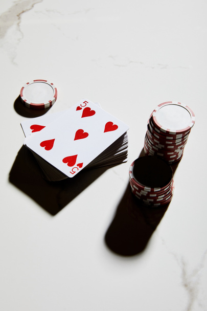 Vista de alto ángulo de fichas de casino con baraja de cartas sobre fondo blanco
 - Foto, imagen