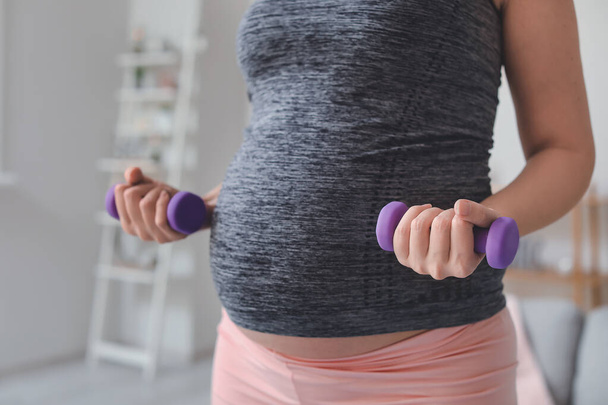 Mooie sportieve zwangere vrouw training met halters thuis, close-up - Foto, afbeelding