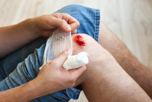 Der Mann heilt die Wunde am Knie zu Hause. Den Verband an den Händen halten - Foto, Bild