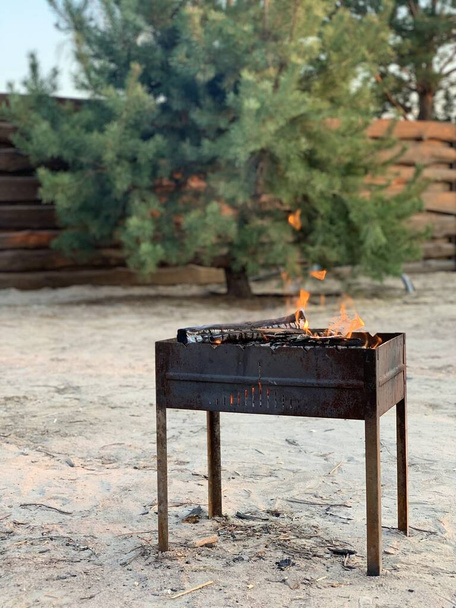 Grigliata calda durante un picnic in cortile. Torrefattore metallico con carbone, in natura. Il fuoco brucia in una griglia pieghevole per cucinare
. - Foto, immagini