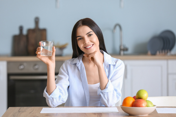 Beautiful young woman drinking water in kitchen - Foto, Bild