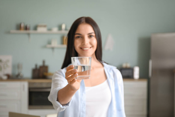 Beautiful young woman drinking water in kitchen - 写真・画像