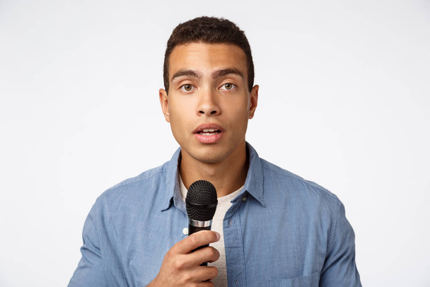 Cute romantic young caucasian guy confess love in front audience, holding microphone and talk with hopeful expression, standing white background, giving speech, singing karaoke - Valokuva, kuva