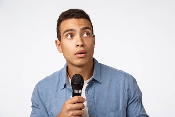 Surprised young man stop speech as hear strange noise, hold microphone, turn right and stare curious or intrigued, standing white background, prepare to sing on stage, worry perform in front audience - Фото, зображення