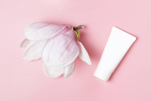 White tube with cream and magnolia flower on a pink background. - Photo, Image