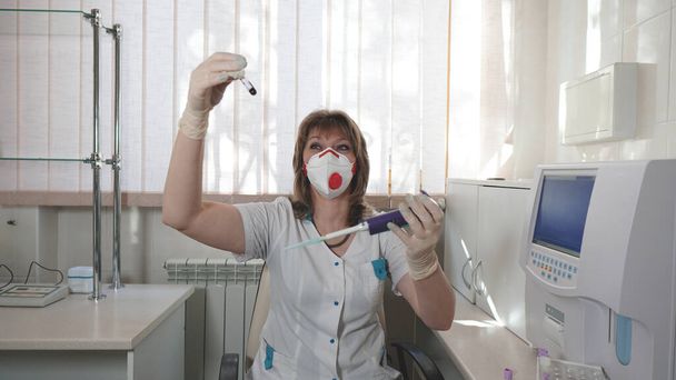Portrét zdravotnického laboranta s červeným chlopeň respirátor z koronaviru v laboratoři pro vyšetřování. . Laborant držící pipetu a testující krevní vzorky - Fotografie, Obrázek