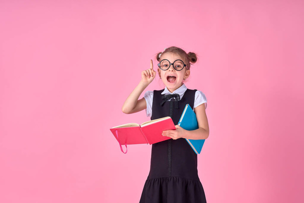 A picture of a schoolgirl with textbook emotionally guessing pointing at something over isolate pink background - Fotó, kép