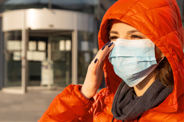 Женщина носит защитную маску от аллергии, вирусов, загрязнения воздуха. Концепция изменения климата. Портрет молодой женщины в медицинской маске из коронавируса в красной куртке на улице
 - Фото, изображение