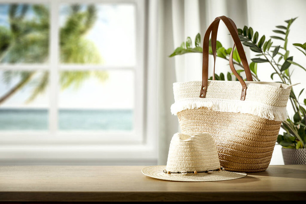 White window and wooden table background with straw hat and straw bag and blue ocean view outside the window. - 写真・画像