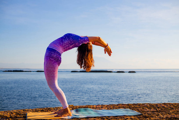Junge Frau, die Yoga praktiziert, steht in Hasta Uttanasana Pose, Ablenkung zurück. Sonnenaufgang Yoga-Praxis. Flexible Wirbelsäule. Selbstversorgungskonzept, gesunder Lebensstil. Yoga-Retreat. Bali, Indonesien - Foto, Bild
