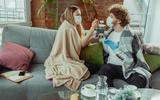 Vrouw en man, paar in beschermende maskers en handschoenen geïsoleerd thuis met coronavirus symptomen - Foto, afbeelding