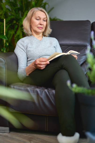 Gelukkig vrouw met een boek in zijn handen ontspannen op haar bank thuis in de woonkamer - Foto, afbeelding
