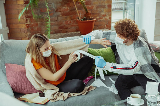 Woman and man, couple in protective masks and gloves isolated at home with coronavirus symptoms - Foto, afbeelding
