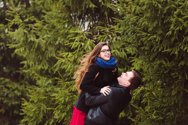 The guy holds a girl on the background of fir trees - Фото, изображение