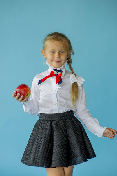 6 éves lány fehér pólóban elszigetelt kék stúdió háttér, csinos európai megjelenésű gyermek pózol beltéri mosolygós pillantást kamera, generációs Z koncepció. Lány iskolás lány egy kék háttér - Fotó, kép