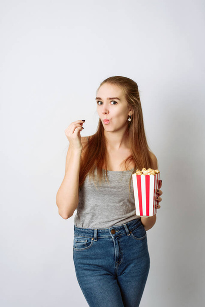 Leuk meisje die popcorn eet, een film kijkt op een grijze achtergrond. Movie viewing concept. - Foto, afbeelding