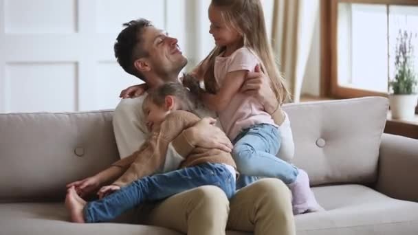 Glücklicher Vater entspannt auf dem Sofa mit niedlichen kleinen Kindern. - Filmmaterial, Video