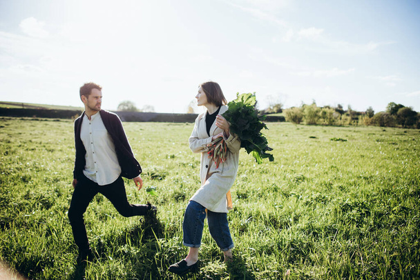 Couple walking in the field in the spring at sunset. Woman holding bouquet. - Fotoğraf, Görsel