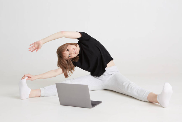 A cool girl does gymnastics remotely at home. Remote training on a laptop. Stay at home leisure  - 写真・画像