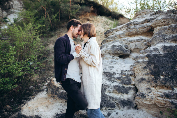 Joven pareja hipster enamorada posando cerca de las rocas al atardecer
 - Foto, Imagen