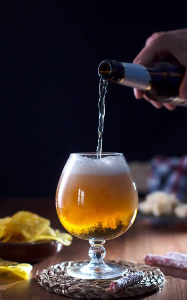 Man pouring craft beer into glass, dark wooden background - Foto, immagini