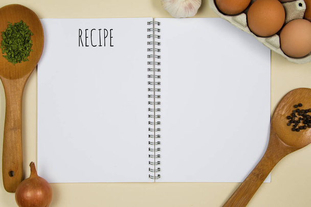 Ξύλινα κουτάλια με μπαχαρικά, αυγά και σκόρδο με κενό σημειωματάριο σελίδα - Φωτογραφία, εικόνα